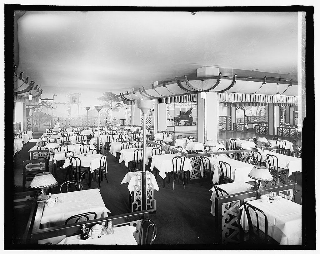 A grand hotel restaurant dining room in the early 1900s — white tablecloths, precise place settings, the front-of-house result of kitchen discipline